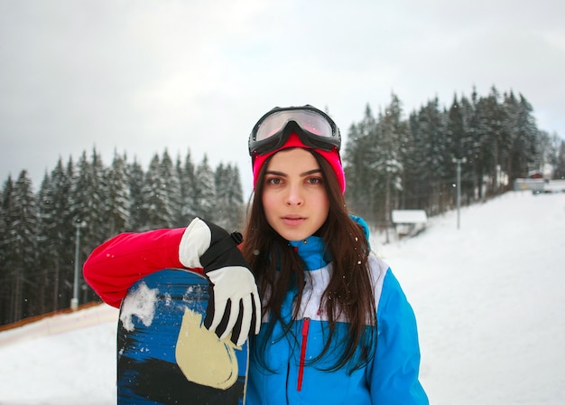 Woman snowboarder in winter at ski resort on background of pine trees