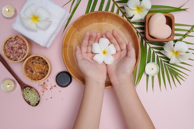 Donna che immerge le mani in una ciotola di acqua e fiori, trattamento spa e prodotto per piedi femminili e spa per le mani, massaggio con ciottoli, acqua profumata di fiori e candele, relax. lay piatto. vista dall'alto.