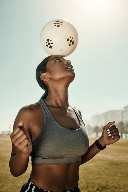 Pallone da calcio donna ed equilibrio sulla testa nell'allenamento campo sportivo campo in erba o club di allenamento fitness giocatore di football donna nera e atleta nella pratica dell'esercizio con obiettivi di benessere o motivazione