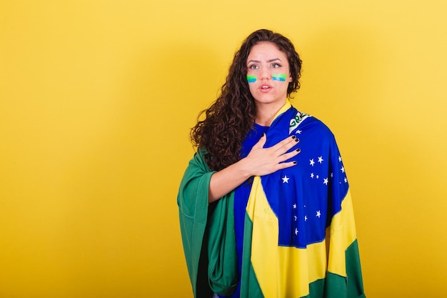 Woman soccer fan fan of Brazil World Cup singing the national anthem hand on chest