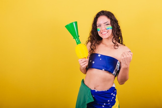 Woman soccer fan fan of brazil world cup wearing flag as a garment celebrating holding horn