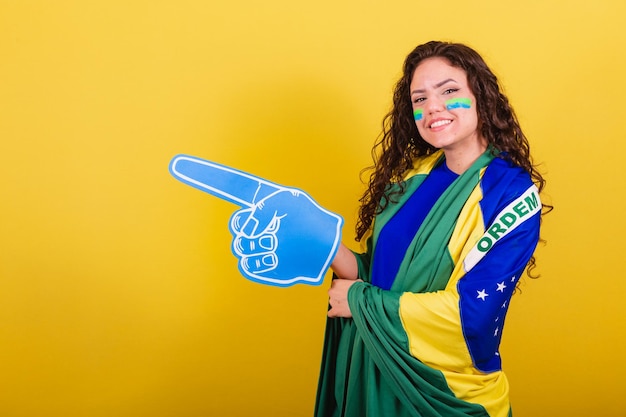 Woman soccer fan fan of brazil world cup wearing foam glove\
pointing to negative space ad text or advertising left side