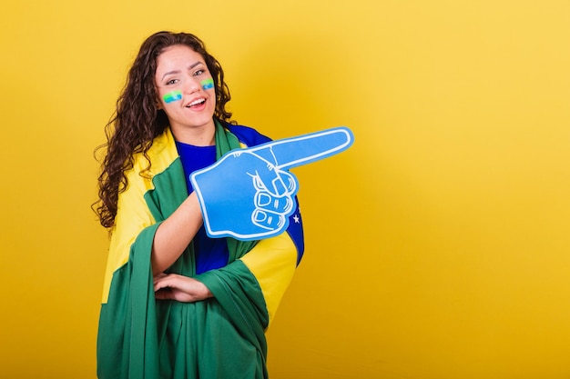 Woman soccer fan fan of brazil world cup wearing foam glove\
pointing to negative space ad text or advertising right side