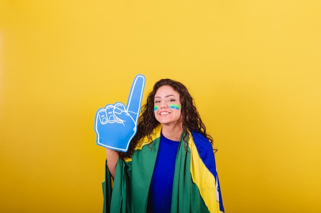 Woman soccer fan fan of brazil world cup wearing foam glove pointing to negative space ad text or advertising up