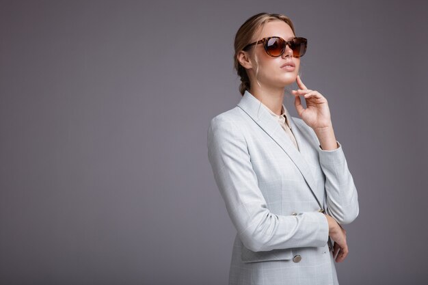 Woman in soft blue suit jacket pants sunglasses Gray background Studio shot Monochrome colors