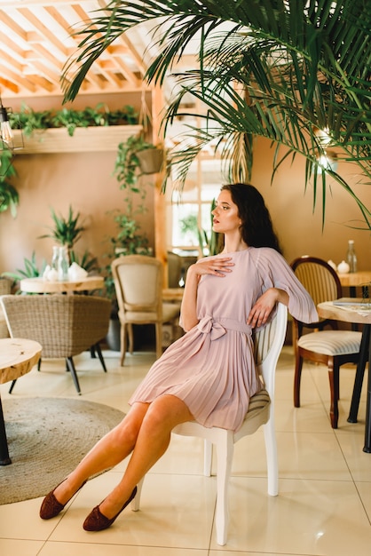 Photo woman in soft pink dress is sitting on the chair and looking to the left side