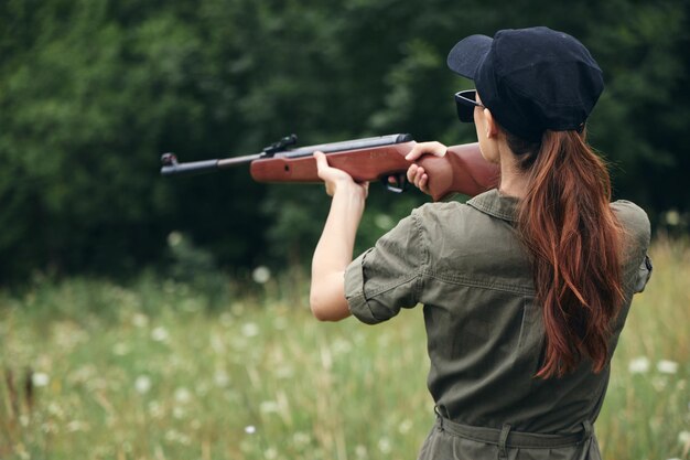 Photo woman soldier holds a gun in his hands aiming rear view weapons green trees on background