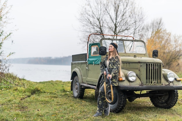 Woman soldier with rifle posing near military car