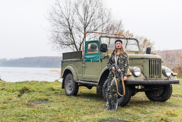 Foto donna soldato con fucile in posa vicino a un'auto militare