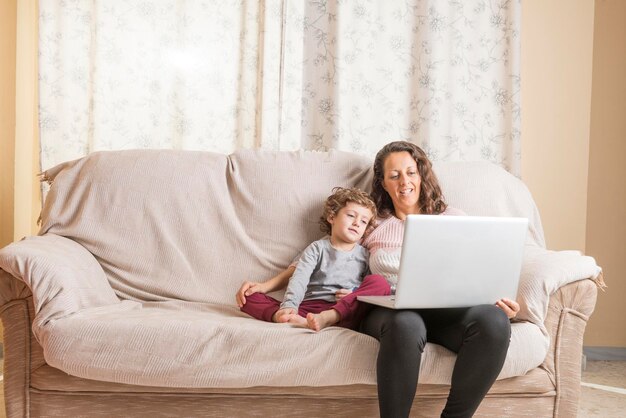 Woman and son with laptop sitting on sofa at home