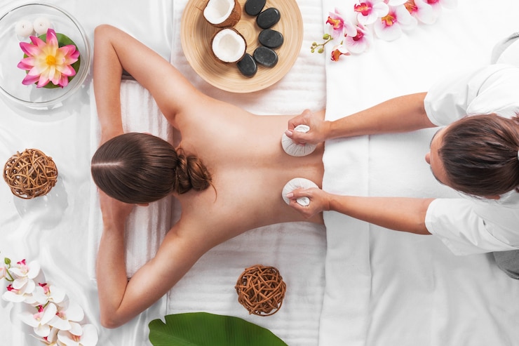 Photo woman at spa thai massage tow view, beauty treatments concept. orchid and lotus flowers coconut stones and herb pouches