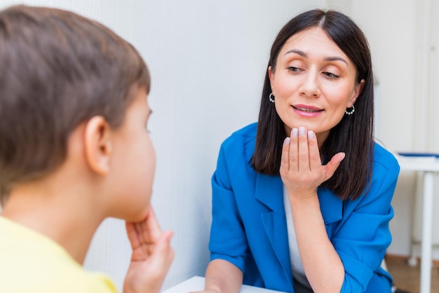 Woman speech therapist helps a boy correct the violation of his speech