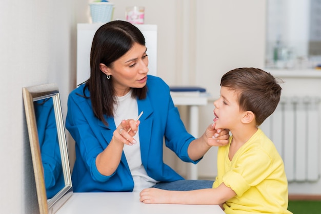 Woman speech therapist helps a child correct the violation of his speech in her office