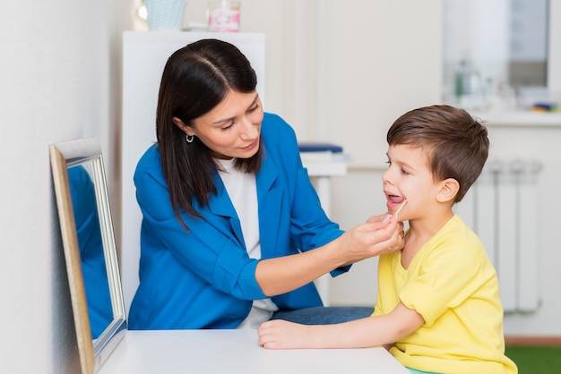 Woman speech therapist helps a child correct the violation of\
his speech in her office