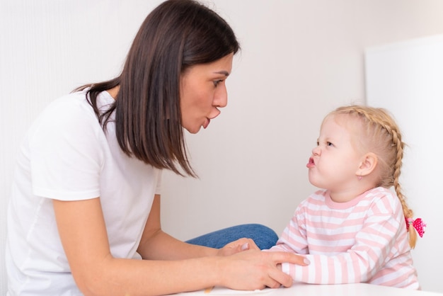 Woman speech therapist helps cute girl to learn correct pronunciation and competent speech in her office
