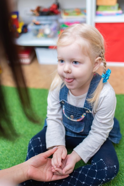 Woman speech therapist helps cute girl to learn correct pronunciation and literate speech