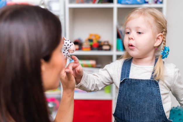 Woman speech therapist helps little girl to correct her speech in her office