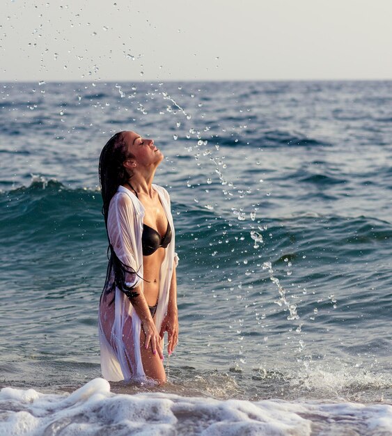 Photo woman splashing water while tossing hair in sea against sky