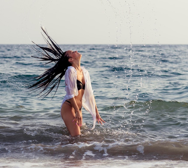 Woman splashing water while tossing hair in sea against sky