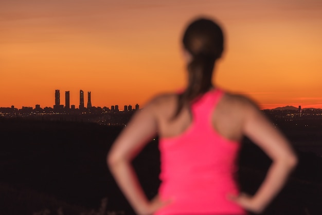 Foto donna sui vestiti di sport che guardano tramonto sopra l'orizzonte della città. l'attenzione è sullo sfondo.