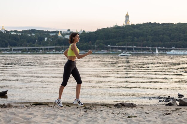 Donna in abbigliamento sportivo al tramonto sulla spiaggia della città in esecuzione