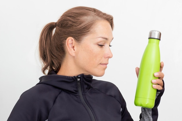 Woman in sportiv dress holding green thermos bottle with water