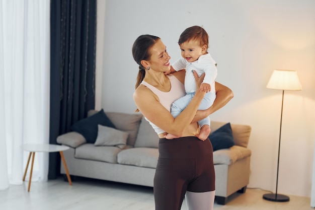 Woman in sportive clothes holding little girl mother with her\
little daughter is at home together