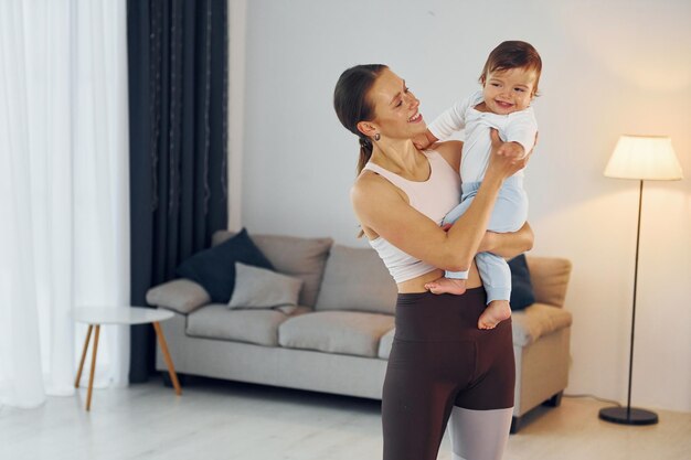 Donna in abiti sportivi che tiene la bambina la madre con la sua piccola figlia è a casa insieme