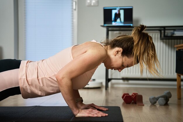 Photo woman in sports clothes does fitness cardio exercises at home using laptop