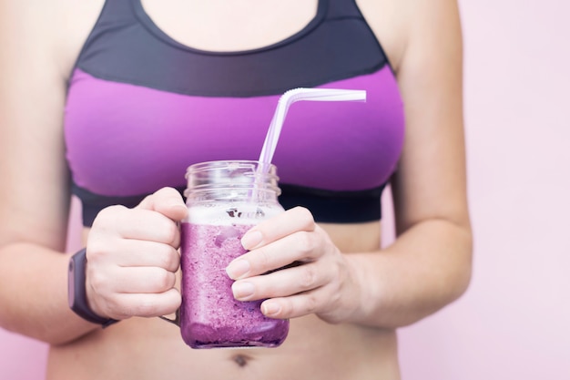 Woman in sports clothes holding fruit blueberries detox smoothie after fitness workout