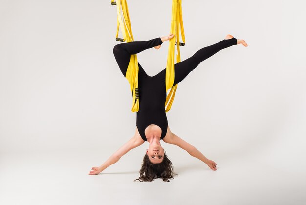 A woman in a sports uniform performs an inverted pose in a hammock. Anti-gravity yoga