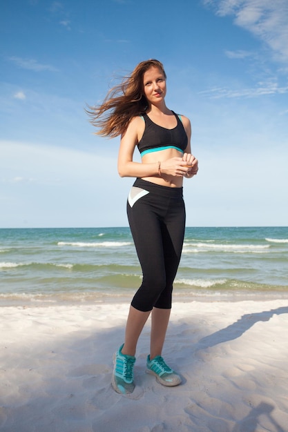 Woman in sports wear posing on the beach near sea