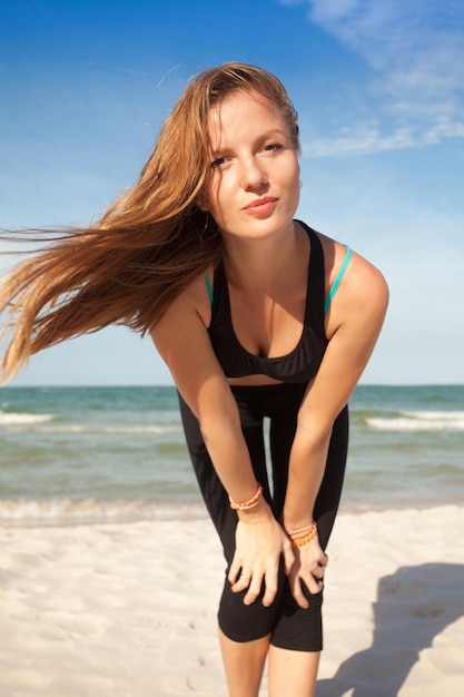 Женщина в спортивной одежде позирует на пляже у моря