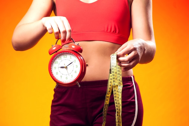 Woman in sportswear holding alarm clock and meter. Fintess time and dieting concept