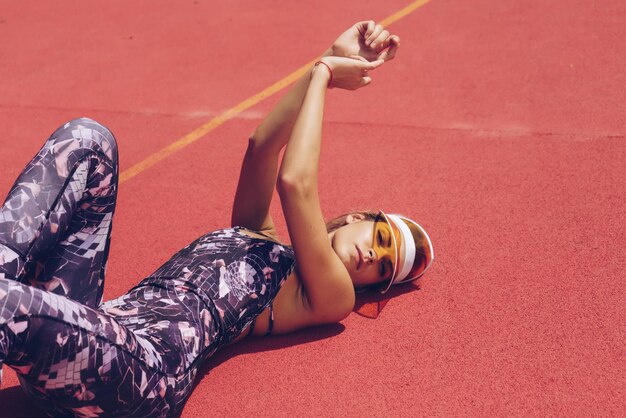 Photo a woman in a sportswear lies on a red surface, wearing a pair of sunglasses.