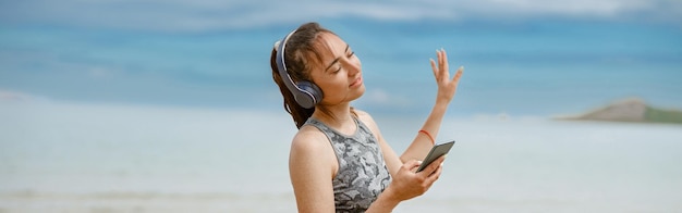 Foto donna in abbigliamento sportivo che ascolta musica in cuffia sulla spiaggia sullo sfondo dell'oceano