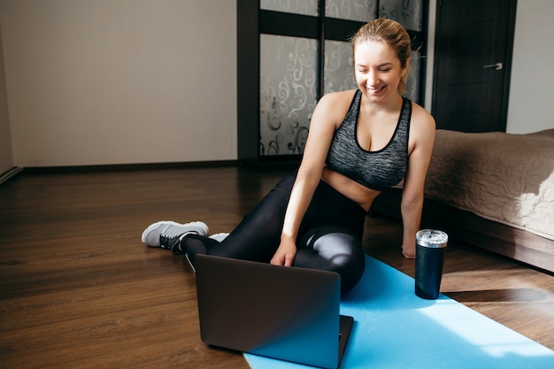 Donna in abiti sportivi seduto sul pavimento e utilizzando un computer portatile