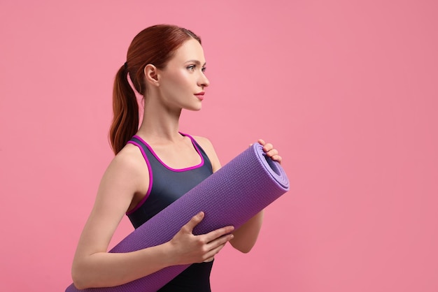 Woman in sportswear with fitness mat on pink background space for text