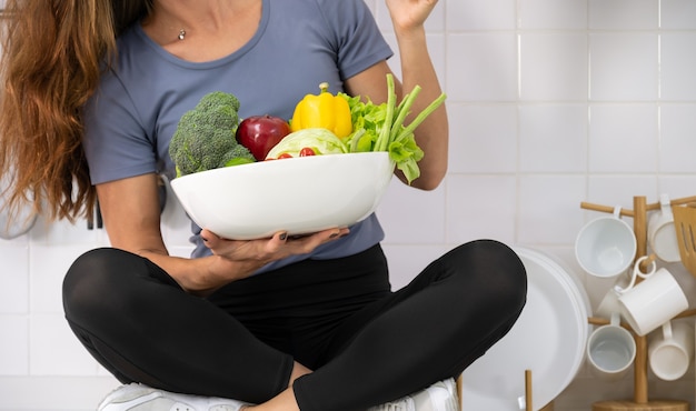 Woman in sportswear with white bowl of  fresh mixed vegetables in her hand.