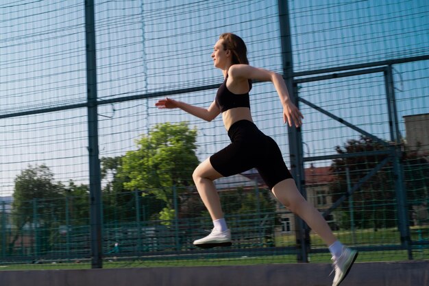 スポーツウェアを着た女性がスポーツスタジアムで運動をしています外でジョギングをしているフィットな女性ウォーミングアップ