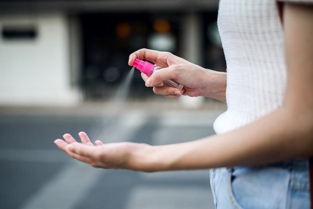 woman spraying  hands with an alcohol-based hand-washing sanitizer spray outdoor to prevent Coronavirus, COVID-19