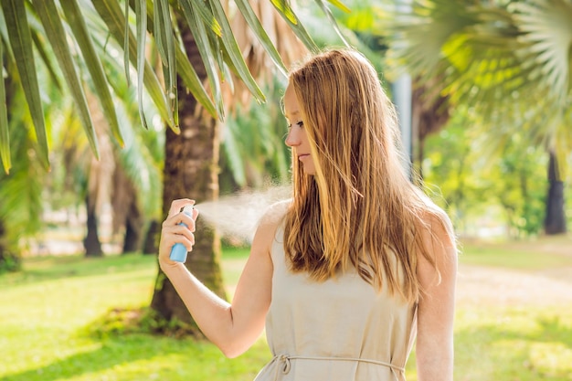 Woman spraying insect repellent on skin outdoor.