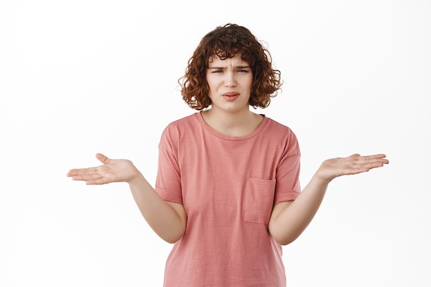 woman spread hands sideways, grimacing and staring questioned, cant understand something strange, standing on white