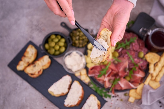 Foto donna che sparge il burro su un pezzo grigliato di baguette con piatto di carne di antipasti italiani sullo sfondo