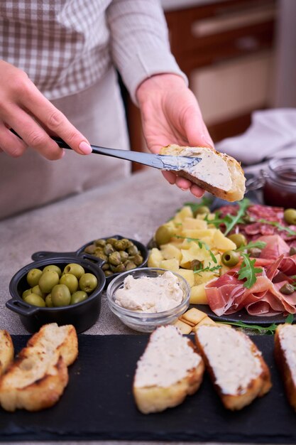 Foto donna che sparge il burro su un pezzo grigliato di baguette con piatto di carne di antipasti italiani sullo sfondo