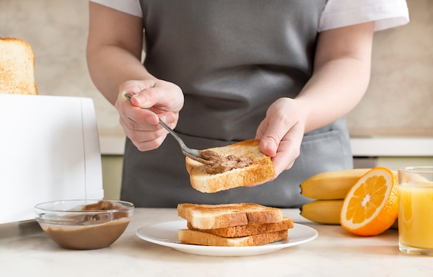 女性は朝食のためにトーストにピーナッツバターを広げます。トースト、ジュース、フルーツを含むヨーロッパ式朝食。