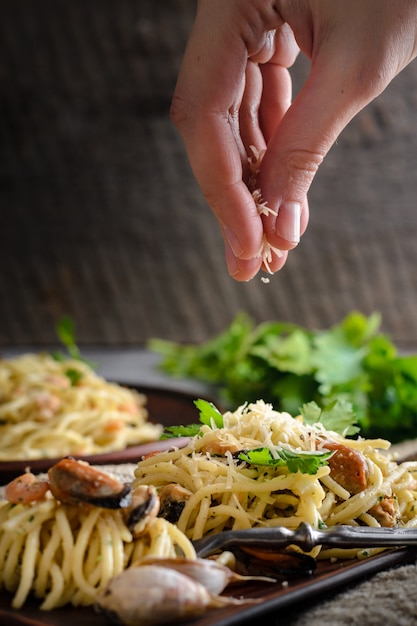 Foto una donna spruzza una pasta di parmigiano con gamberetti e cozze in salsa cremosa.