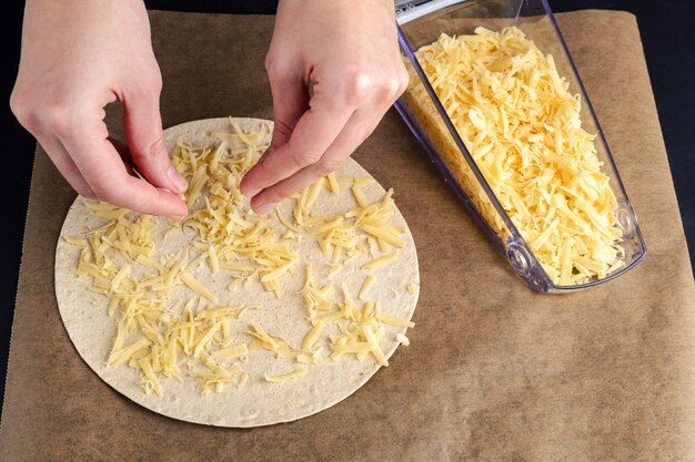 A woman sprinkles a tortilla with cheese