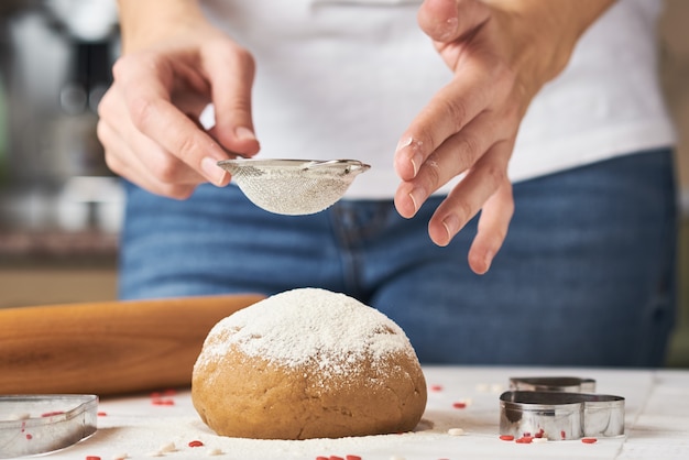 Photo woman sprinkling flour over fresh dough on kitchen table