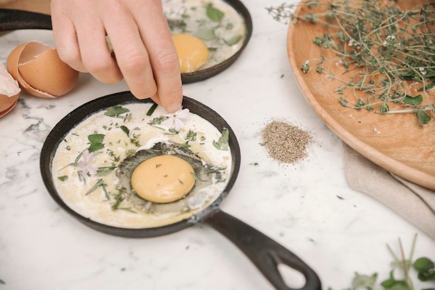 A woman sprinkling herbs over a fresh egg in a pan